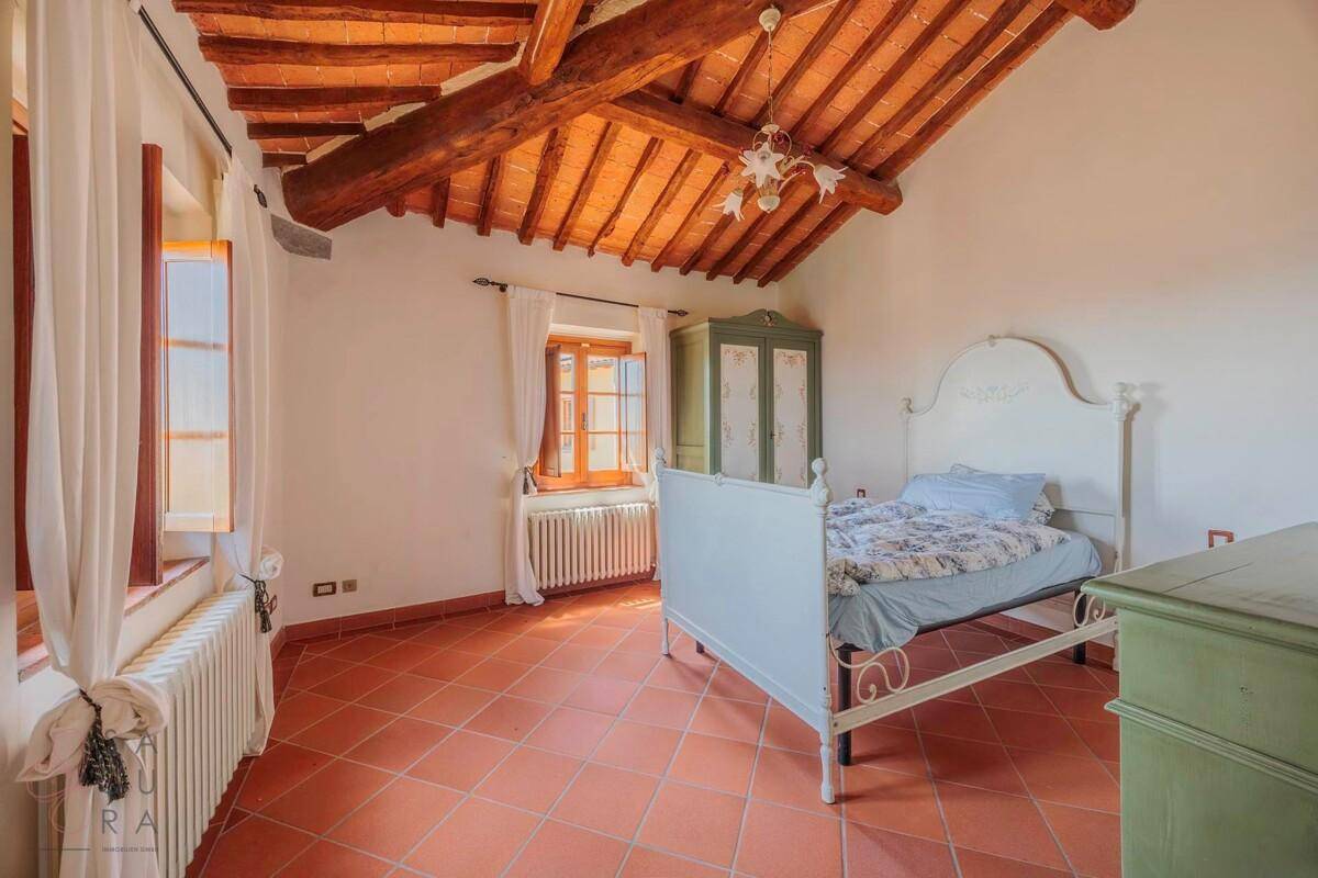 Schlafzimmer mit weißem Bettgestell, Terrakottaboden und sichtbaren Holzbalken unter dem Dach.