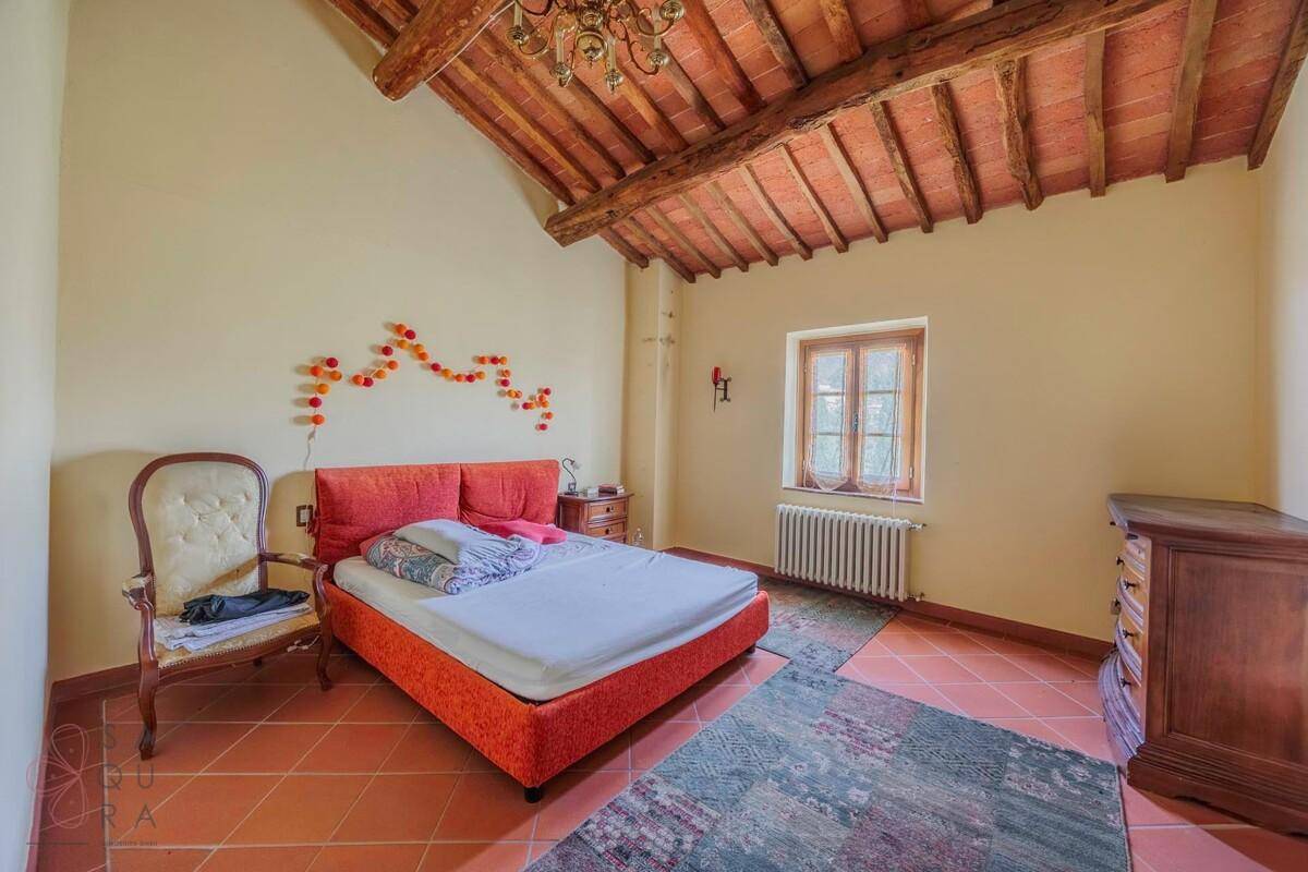 Schlafzimmer mit rotem Bett, Terrakottaboden und charakteristischer Holzbalkendecke unter dem Dach.