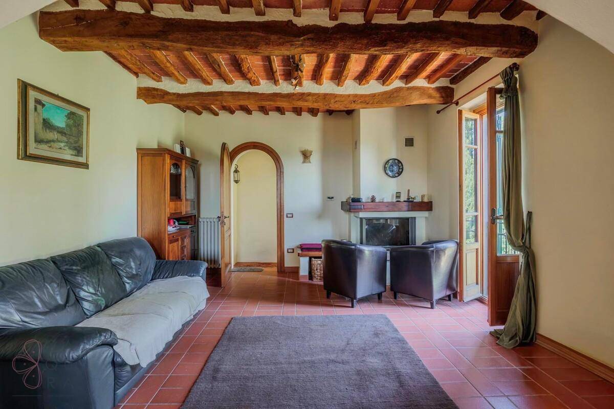 Wohnzimmer mit Kamin, bequemen Sofas und rustikaler Holzbalkendecke sowie Balkonzugang.