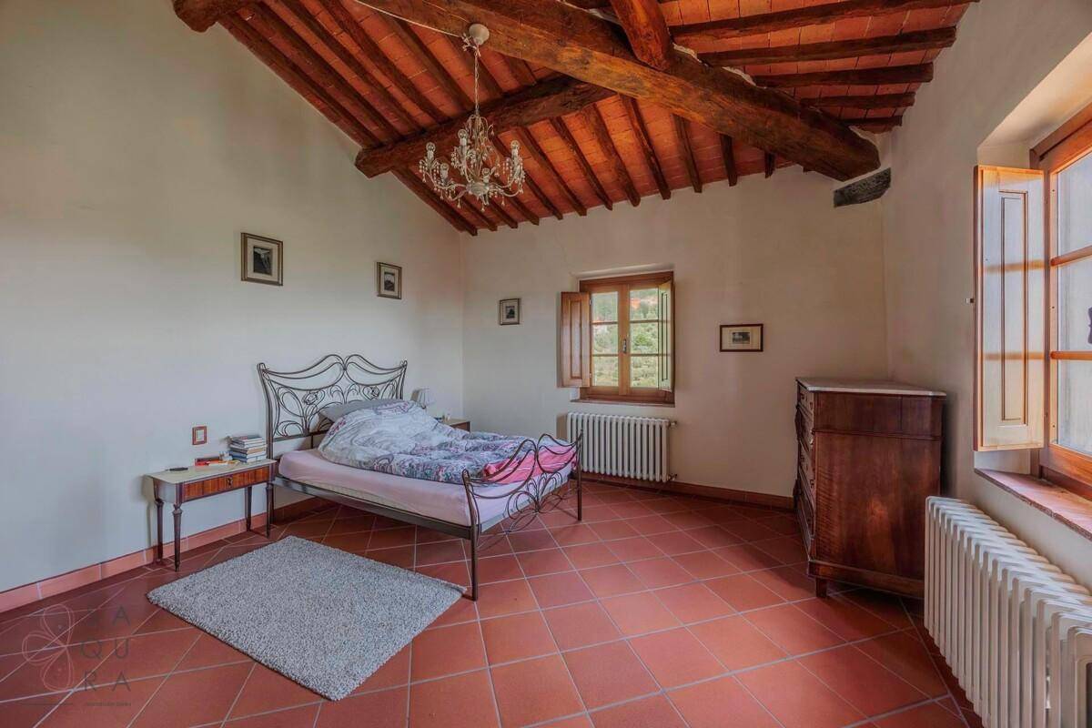 Helles Schlafzimmer mit schmiedeeisernem Bett, Terrakottaboden und rustikaler Holzbalkendecke.