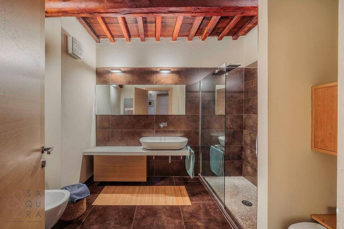 Modernes Badezimmer mit begehbarer Dusche, Einzelwaschbecken und Holzbalkendecke.