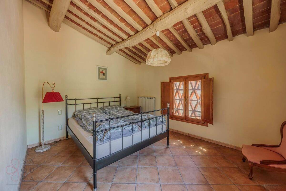 Helles Schlafzimmer mit schmiedeeisernem Bett, Terrakottaboden und sichtbaren Holzbalken.