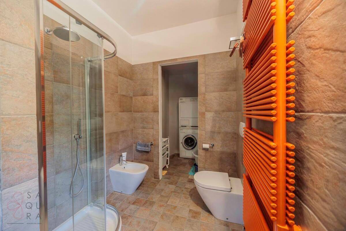 Funktionales Badezimmer mit Duschkabine, WC, Bidet und Waschmaschinen im Hintergrund.