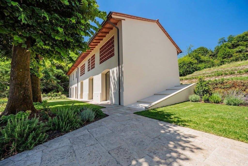 Seitenansicht des Hauses mit gepflastertem Weg, Rasenfläche und Treppe zum oberen Bereich.