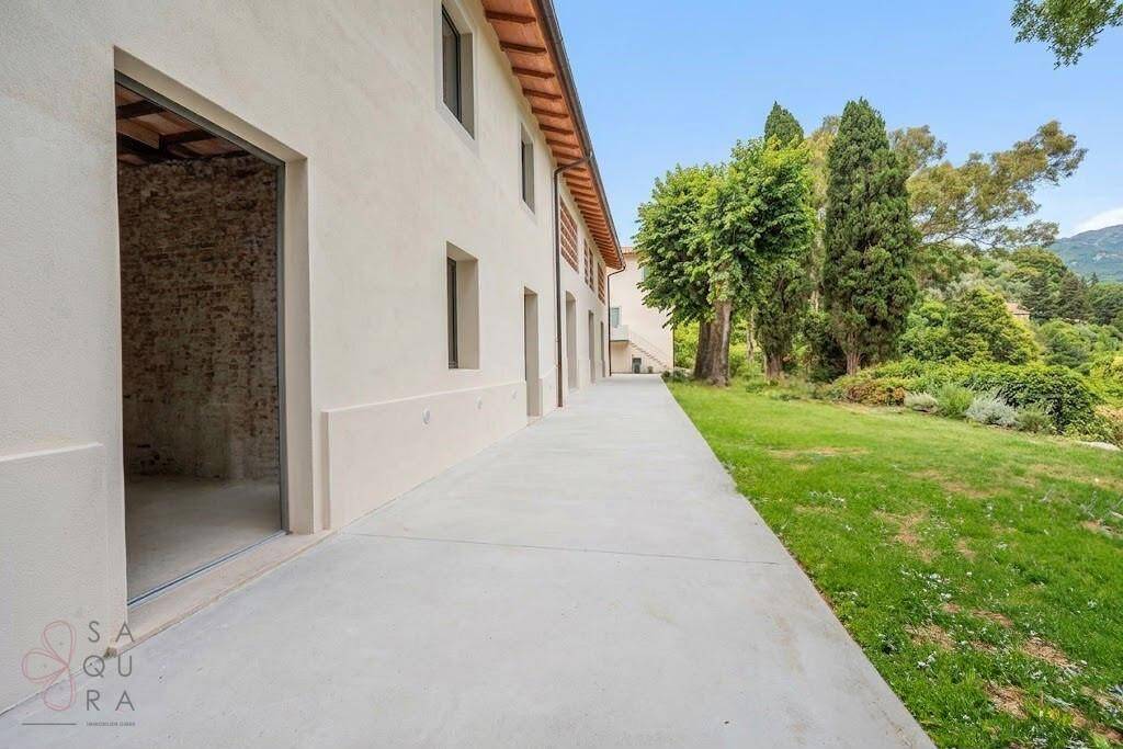 Lange Seitenansicht des Hauses mit Betonweg und offenem Eingangsbereich, umgeben von Grün.