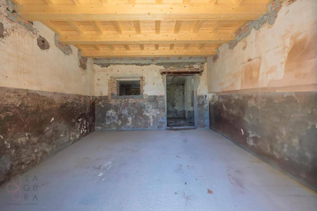 Langer, unfertiger Raum mit rohen Wänden, Holzbalkendecke und kleiner Fensteröffnung.