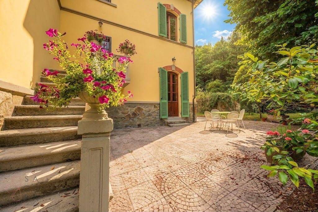 Sonniger Terrassenbereich mit gepflastertem Boden, Gartenmöbeln und blühenden Pflanzen.