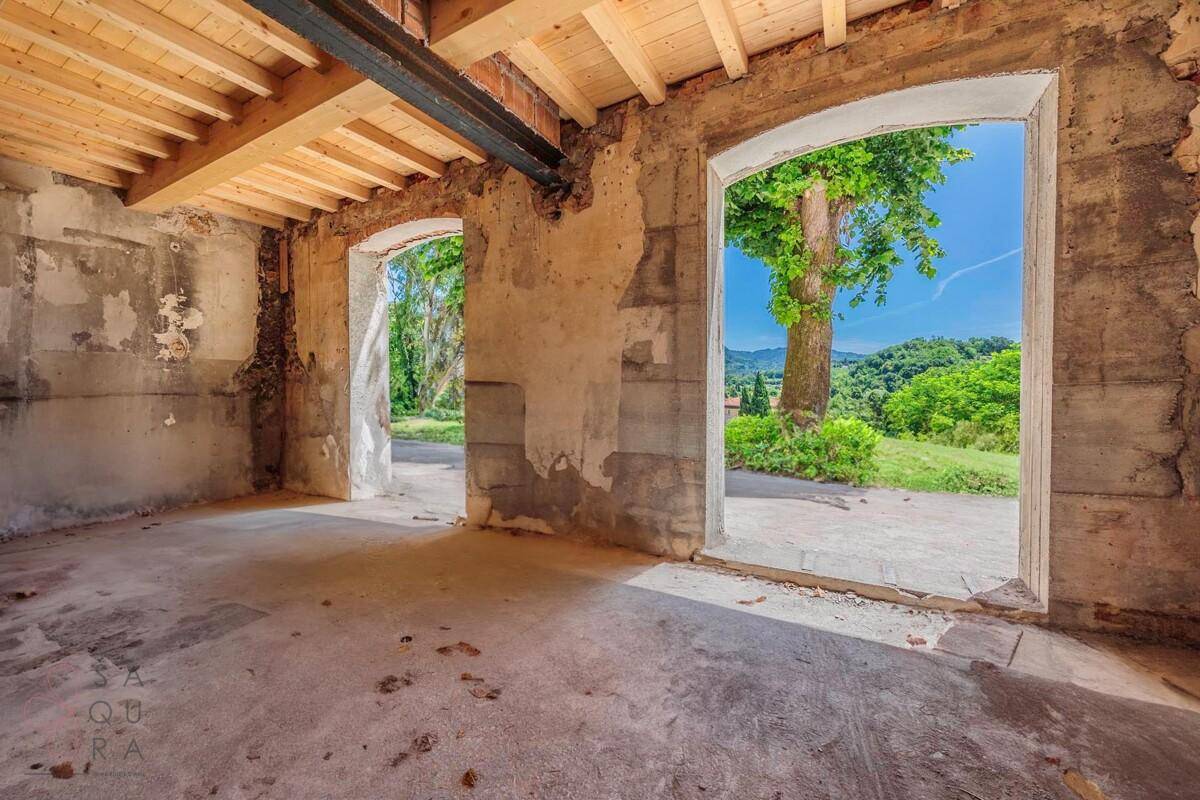 Unfertiger Raum mit Holzbalkendecke und zwei großen Bögen, die den Blick ins Grüne freigeben.