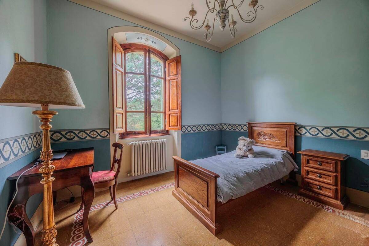 Kinderzimmer mit blau gestrichenen Wänden, Einzelbett und einem Schreibtisch am großen Fenster.