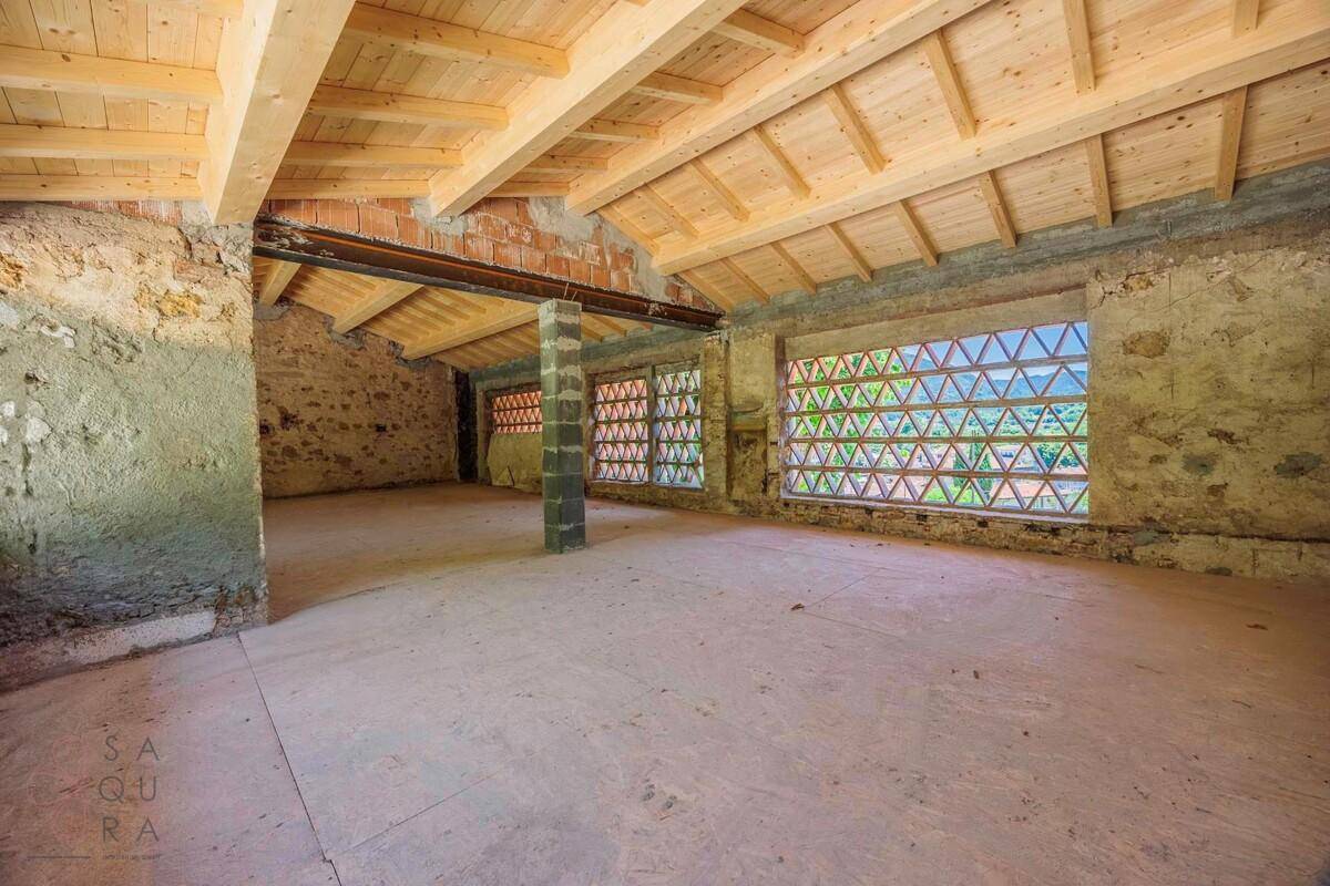 Geräumiger unfertiger Raum mit Holzbalkendecke, unverputzten Wänden und gemusterten Fensteröffnungen.