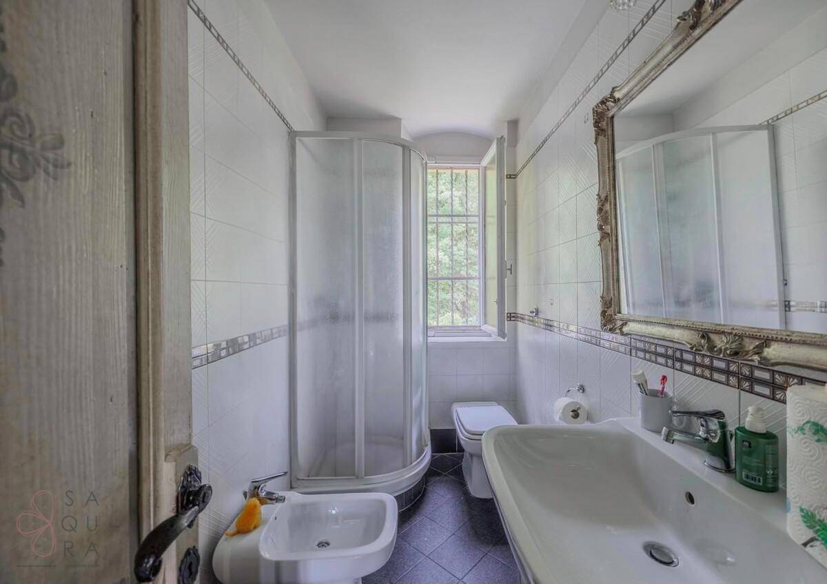 Badezimmer mit Duschkabine, Bidet, Waschbecken und einem Fenster für natürliche Belüftung.
