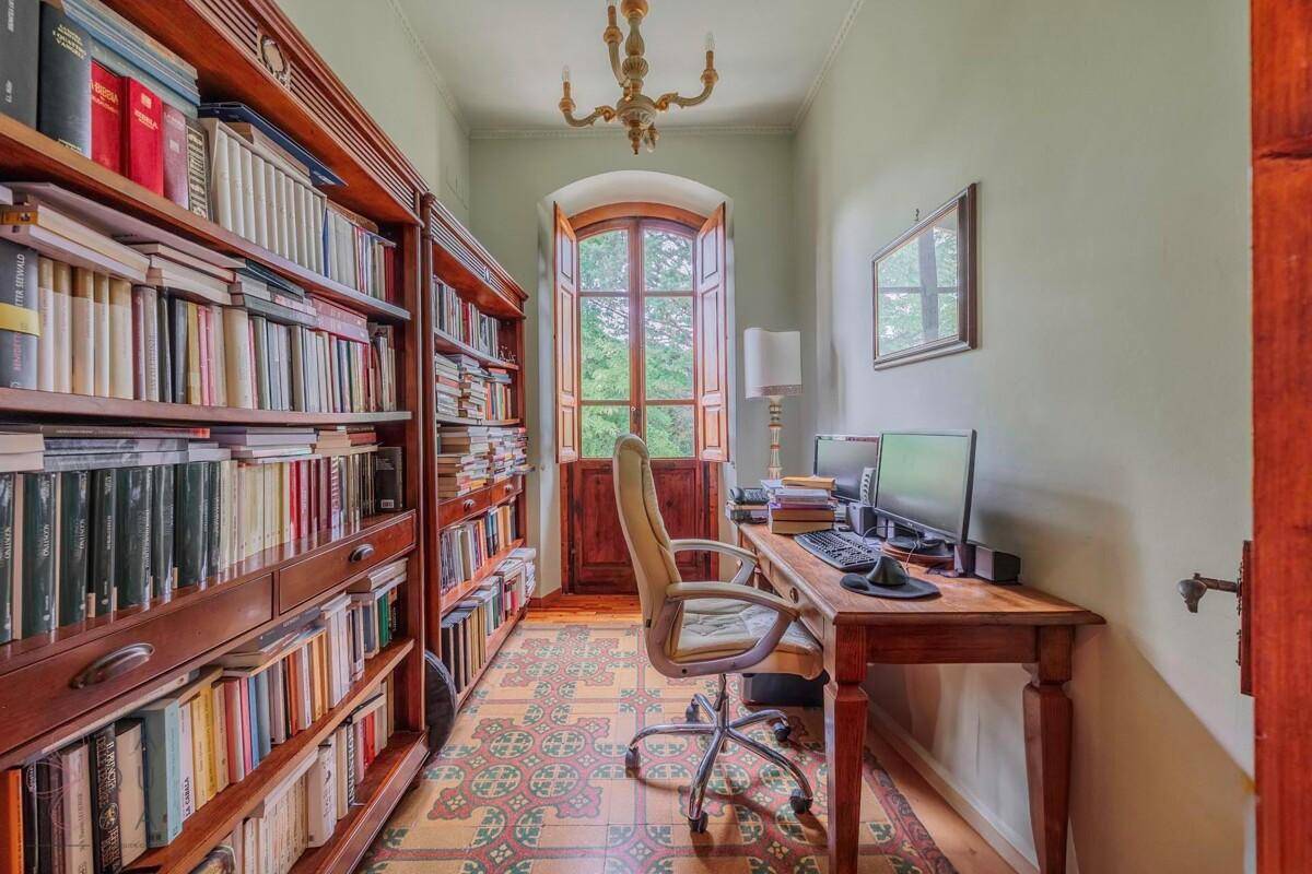 Gemütliches Arbeitszimmer mit großen Holzregalen voller Bücher und einem Schreibtisch am Fenster.