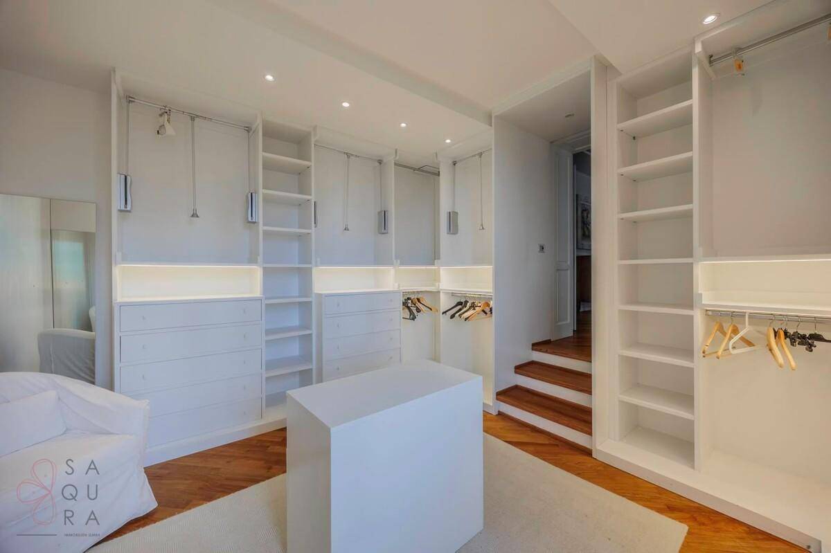 Geräumiger begehbarer Kleiderschrank mit weißen Einbauschränken und Holzfußboden.