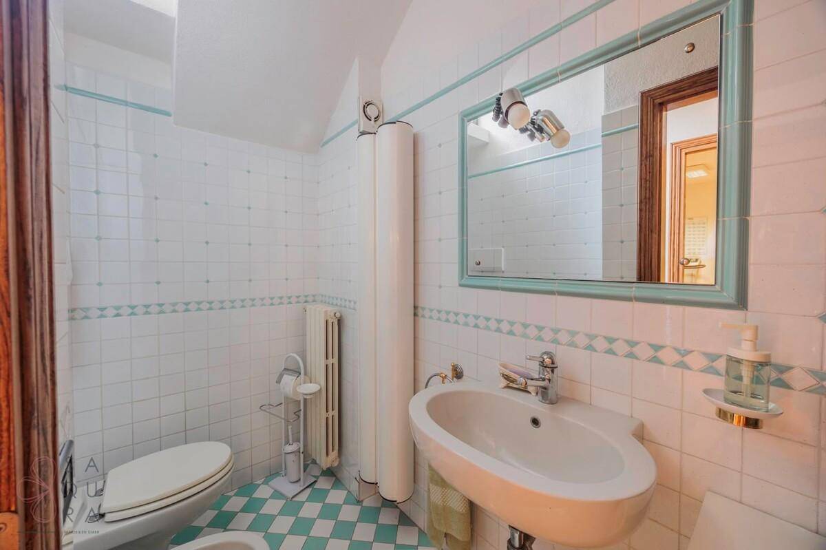 Kleines Badezimmer mit weißen und blauen Fliesen, Waschbecken und WC.