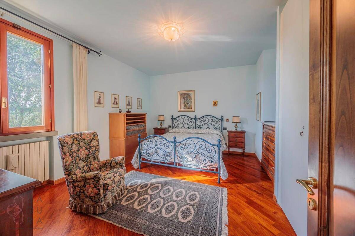 Schlafzimmer mit Holzboden, blauem Metallbett und einem Sessel mit Blumenmuster.