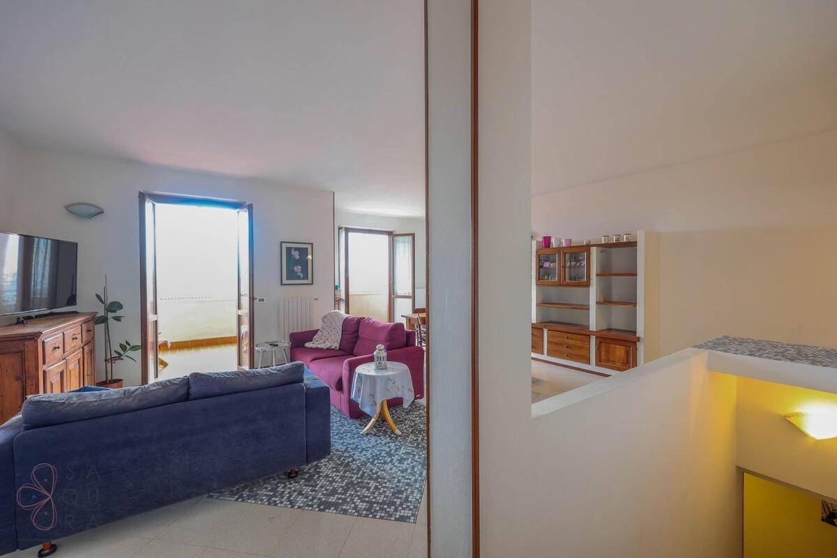 Blick vom Treppenabsatz in den hellen Wohnbereich mit Sofas und Zugang zum Balkon.