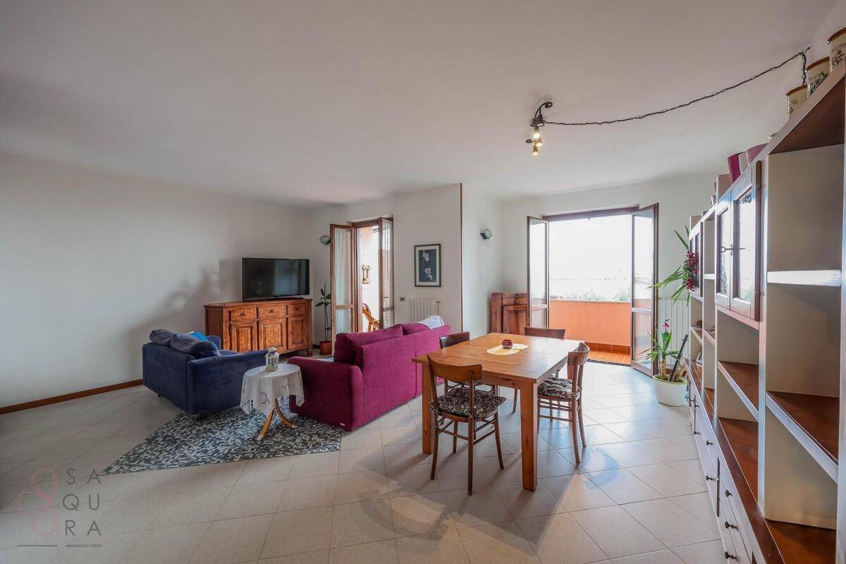 Geräumiger Wohn-Essbereich mit Fliesenboden, bequemen Sofas und Zugang zum Balkon.