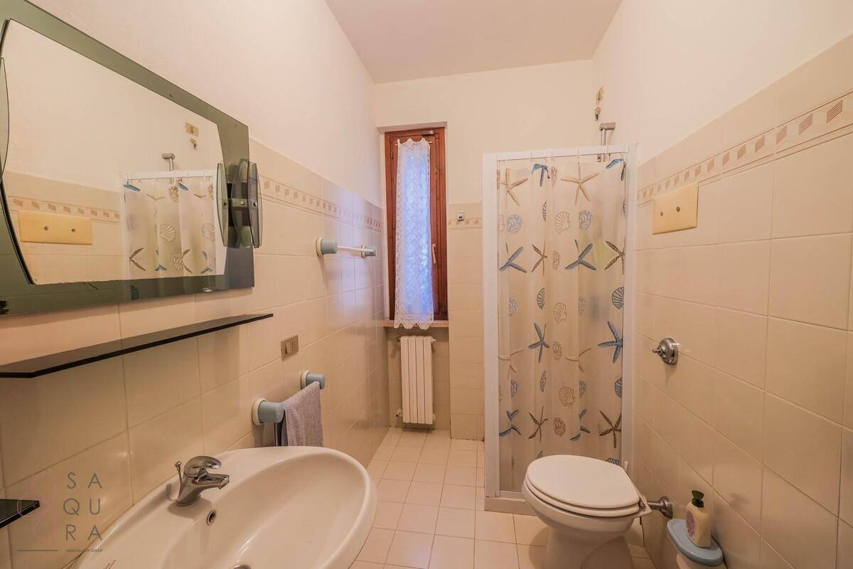 Badezimmer mit Duschkabine, WC, Waschbecken und großem Spiegel, hell gefliest.