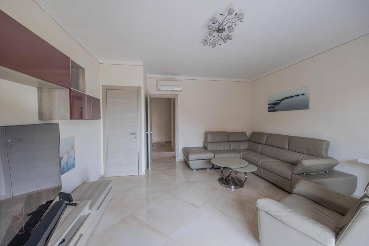 Geräumiges Wohnzimmer mit Ecksofa, Fliesenboden und moderner Wanddekoration.