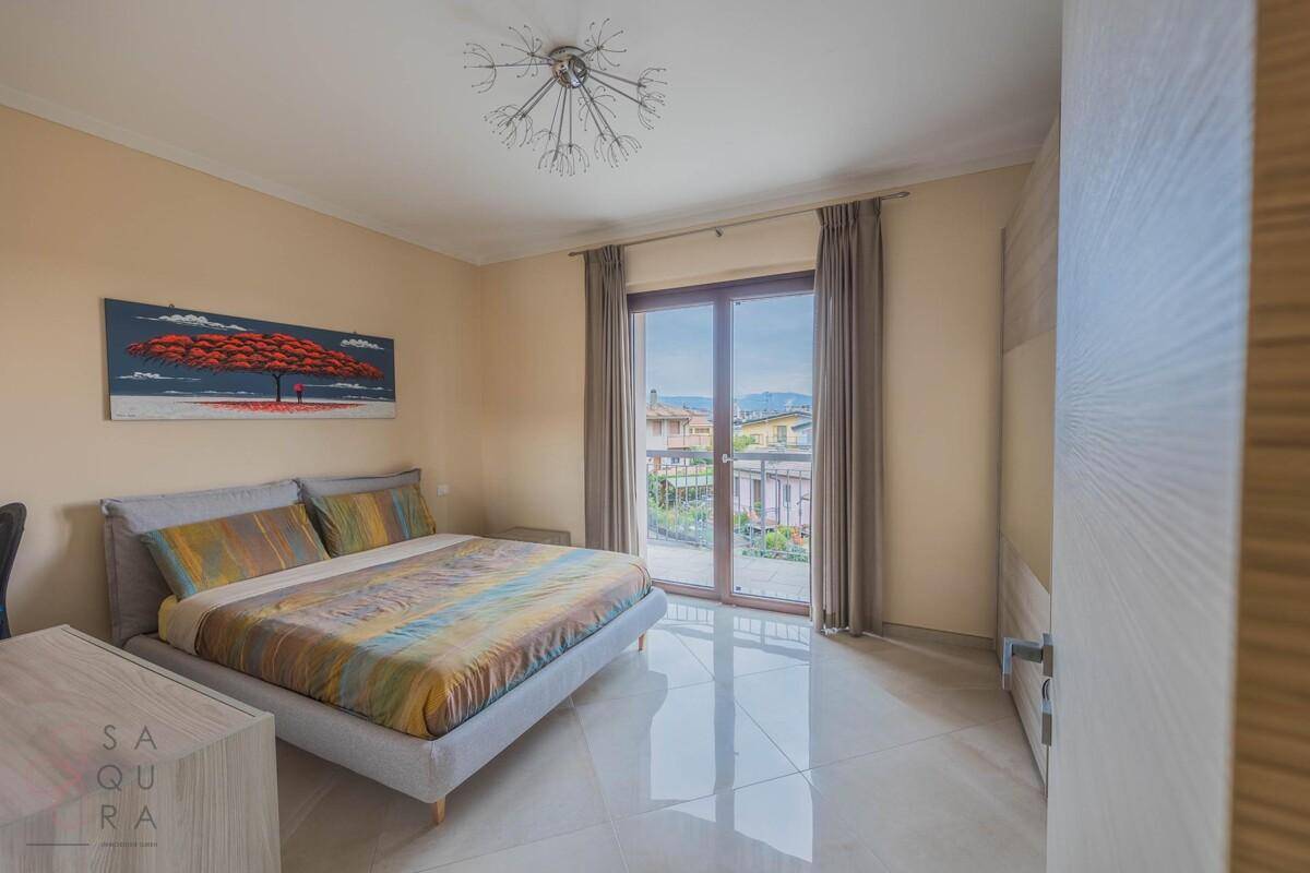 Schlafzimmer mit Doppelbett, Fliesenboden und großem Fenster mit Balkonzugang.