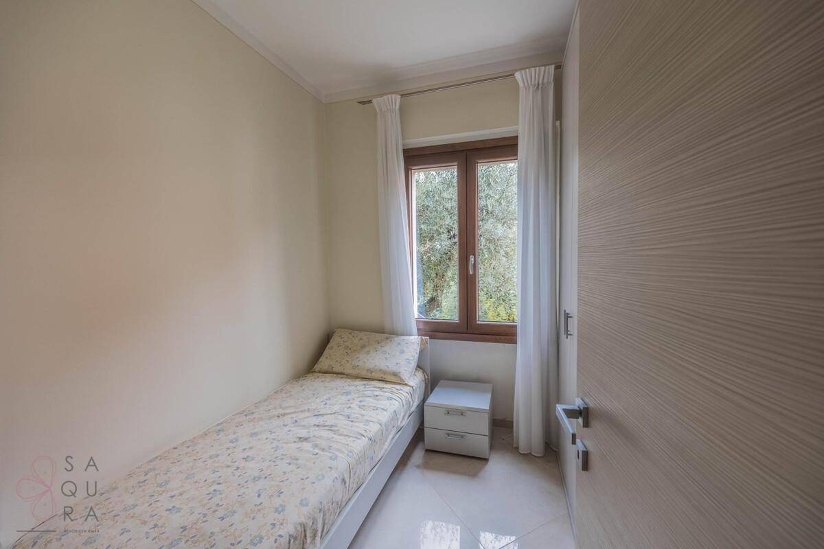 Kleines Schlafzimmer mit Einzelbett, Fliesenboden und Fenster mit Blick ins Grüne.