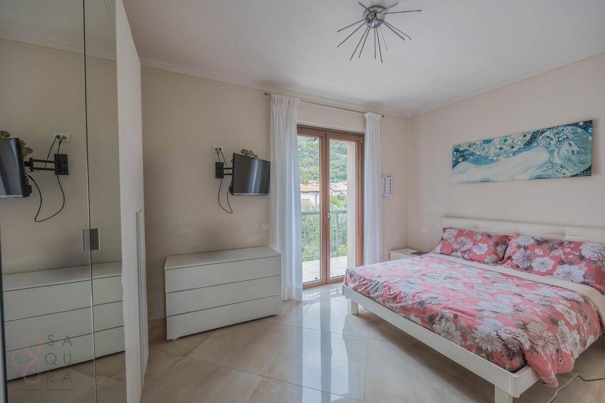 Schlafzimmer mit Doppelbett, Fliesenboden und Balkontür, die viel Licht hereinlässt.