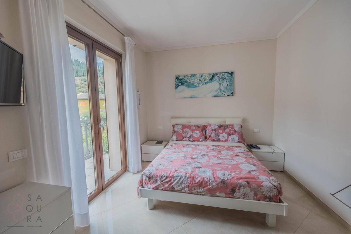 Helles Schlafzimmer mit Doppelbett, Fliesenboden und direktem Zugang zum Balkon.