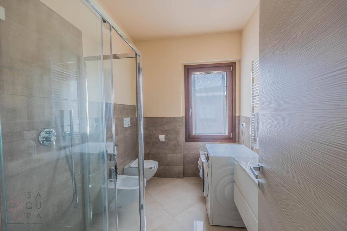 Helles Badezimmer mit Dusche, Waschmaschine und Fenster für natürliche Belüftung.