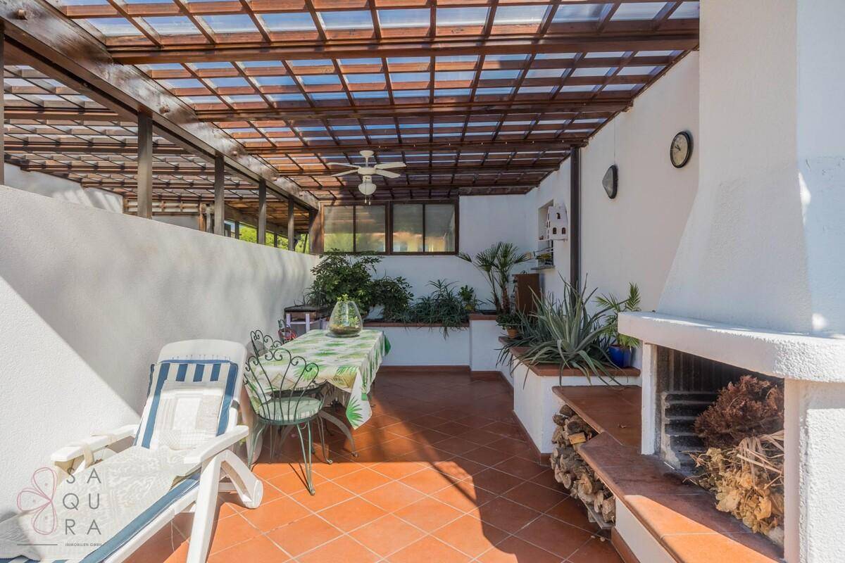 Überdachte Terrasse mit Essbereich, integriertem Grill und mediterranen Pflanzen.