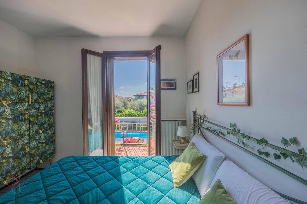 Schlafzimmer mit Balkonzugang, Blick auf den Pool und die grüne Umgebung.