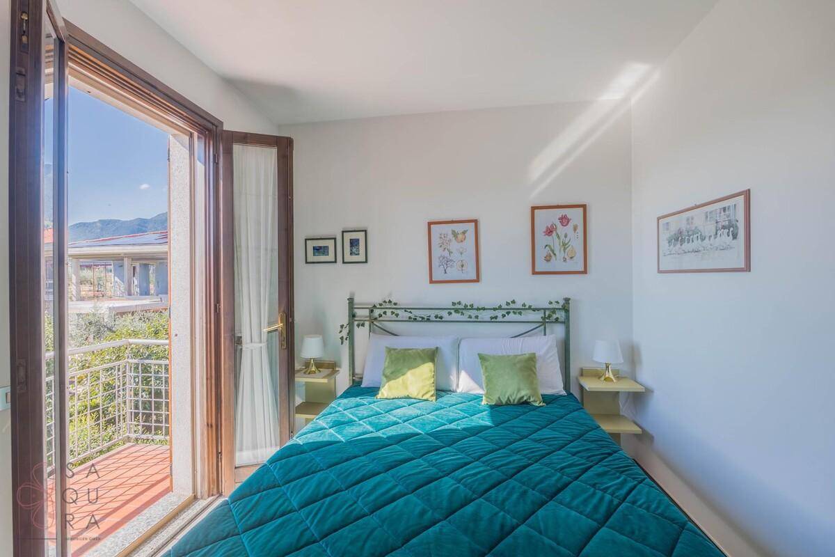Gemütliches Schlafzimmer mit Balkonzugang, Fliesenboden und Blick auf die Umgebung.