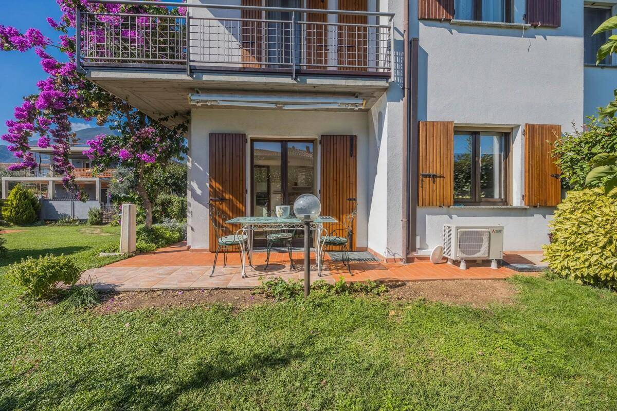 Kleine Terrasse am Haus mit Essgruppe, umgeben von Grün und Blick auf den Garten.