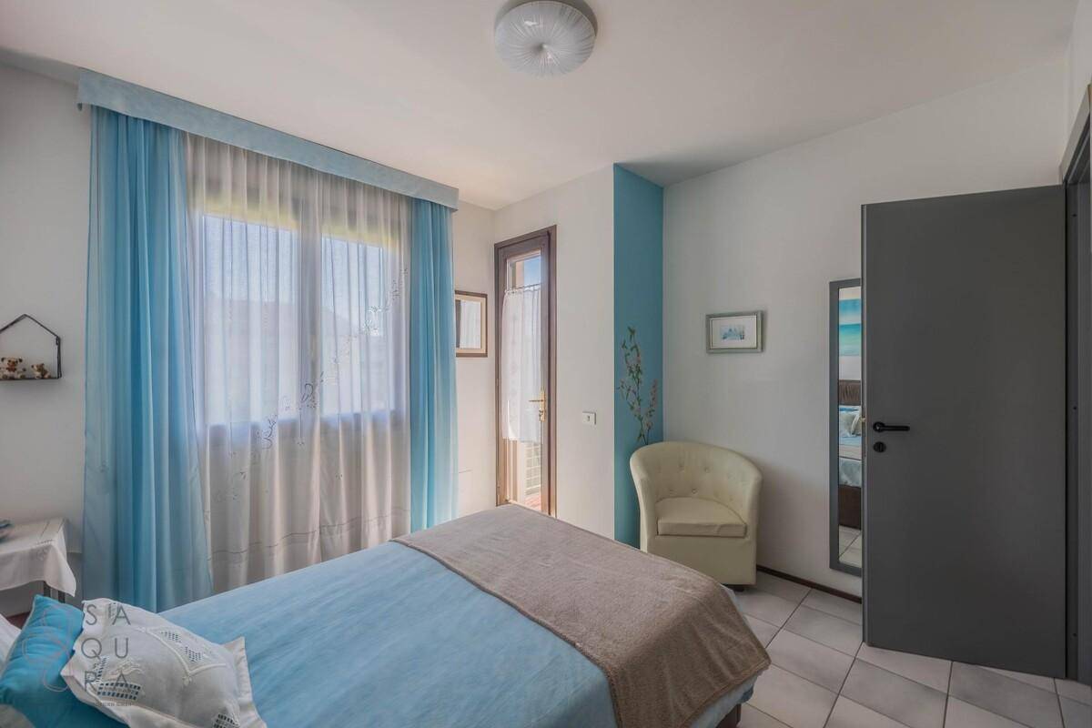 Helles Schlafzimmer mit Balkonzugang, blauen Vorhängen und einem Sessel.
