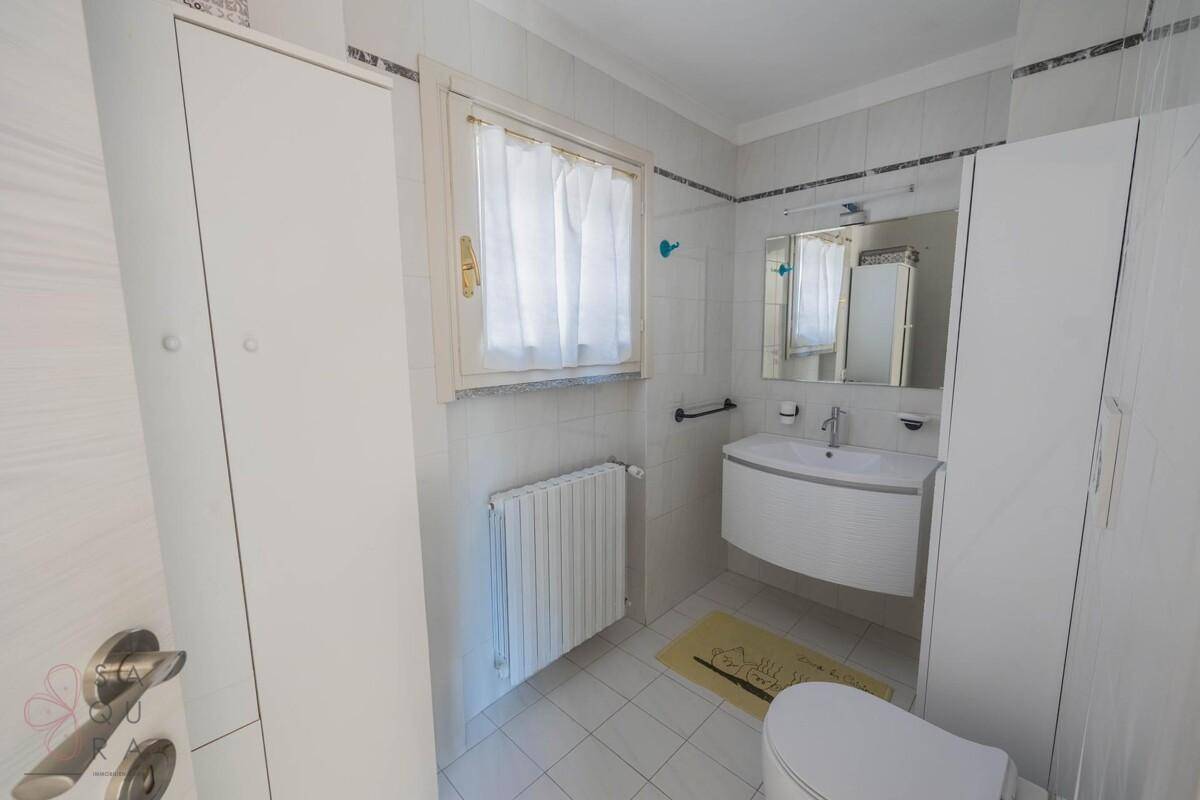 Helles Badezimmer mit Fenster, Waschbecken und weißen Schränken.
