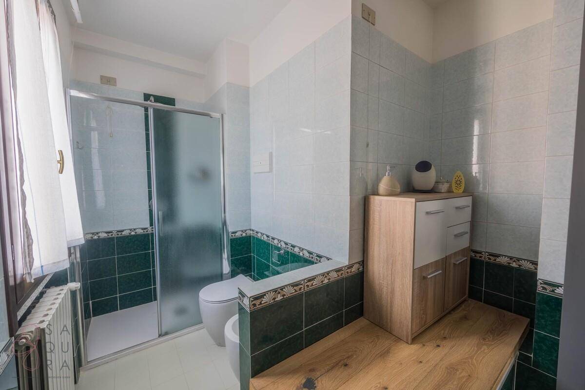 Badezimmer mit Duschkabine, Bidet und grünen Fliesen an den Wänden.