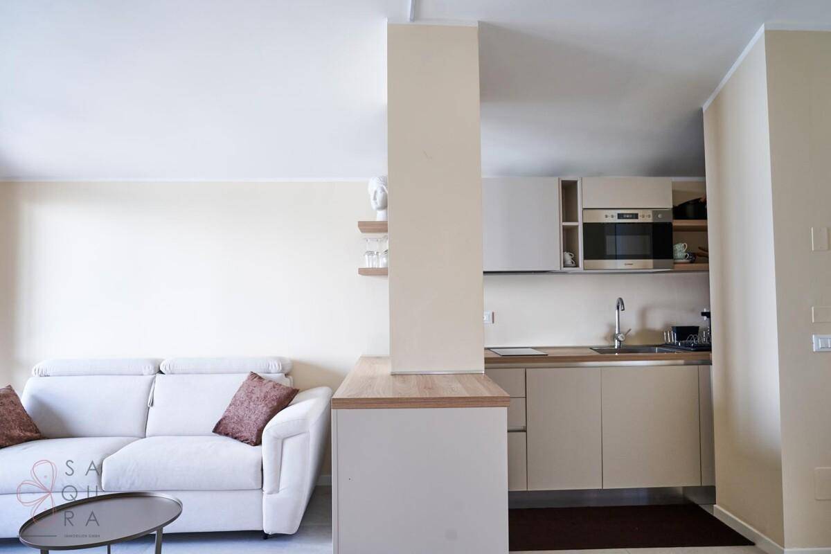 Heller Wohnbereich mit Sofa und integrierter Küchenzeile, modern und funktional eingerichtet.