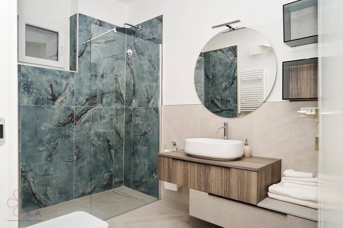 Elegantes Badezimmer mit runden Spiegel, begehbarer Dusche und modernem Waschtisch.