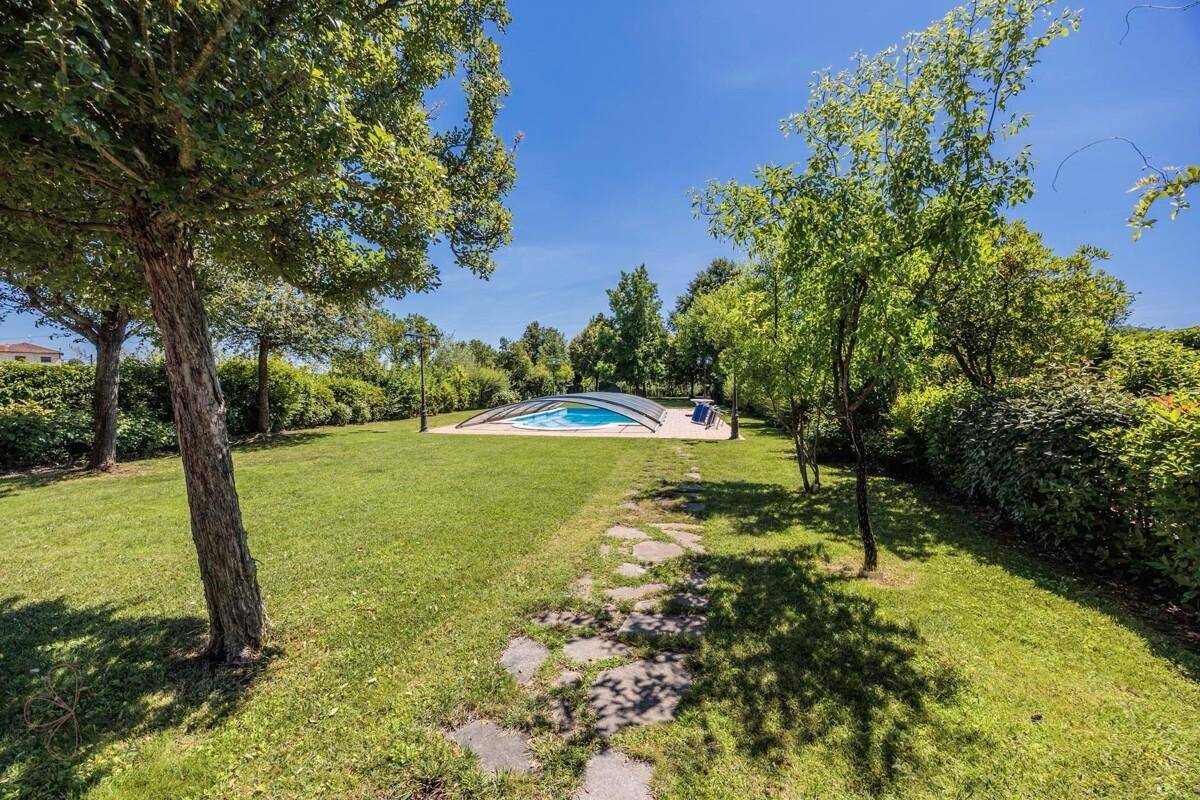 Großer, gepflegter Garten mit Rasenflächen, Bäumen und einem Weg zum Poolbereich.