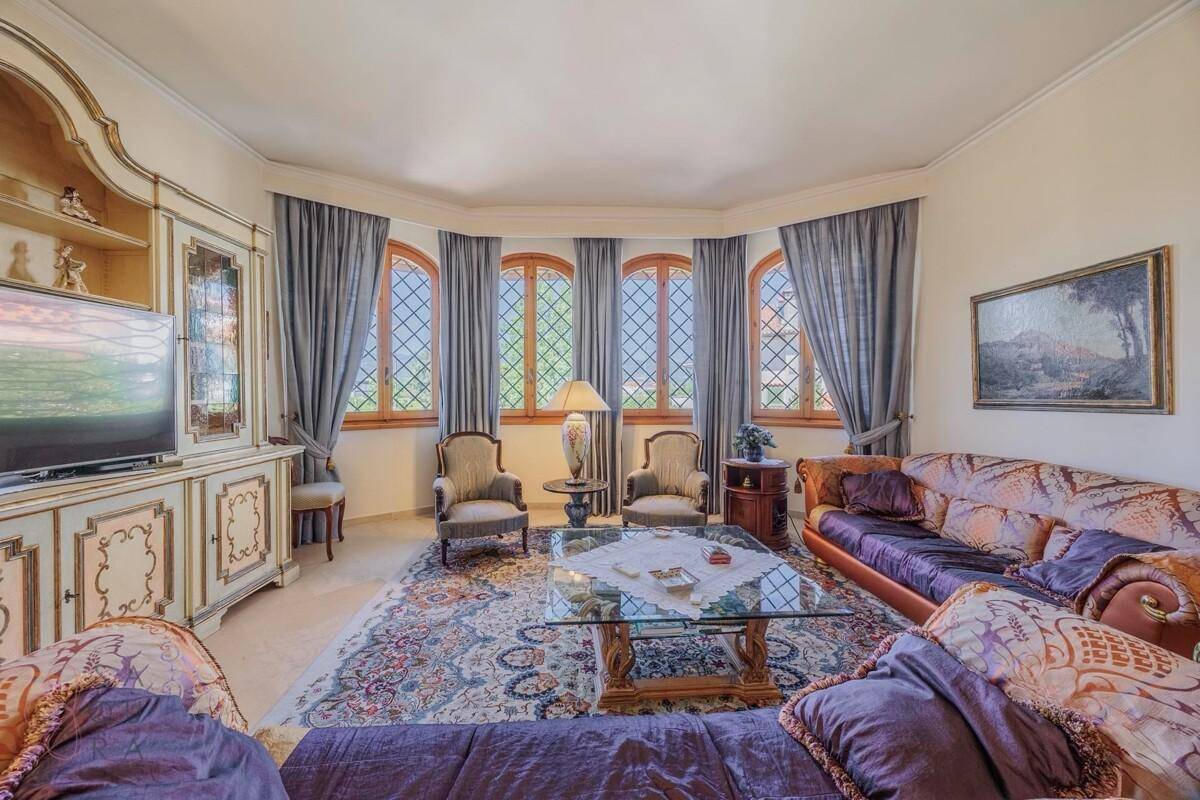 Klassisches Wohnzimmer mit bequemen Sofas, Teppich und großen Fenstern mit Blick ins Grüne.