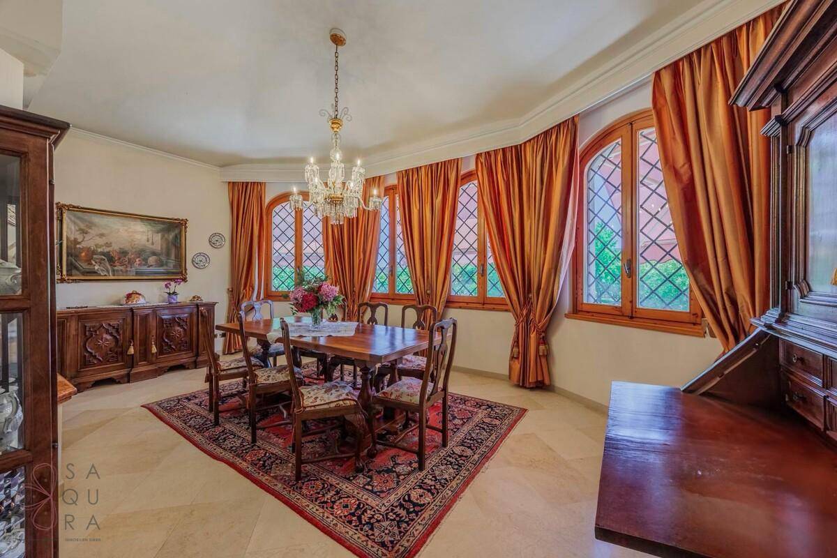 Elegantes Esszimmer mit großem Holztisch, Kronleuchter und mehreren hohen Bogenfenstern mit Vorhängen.