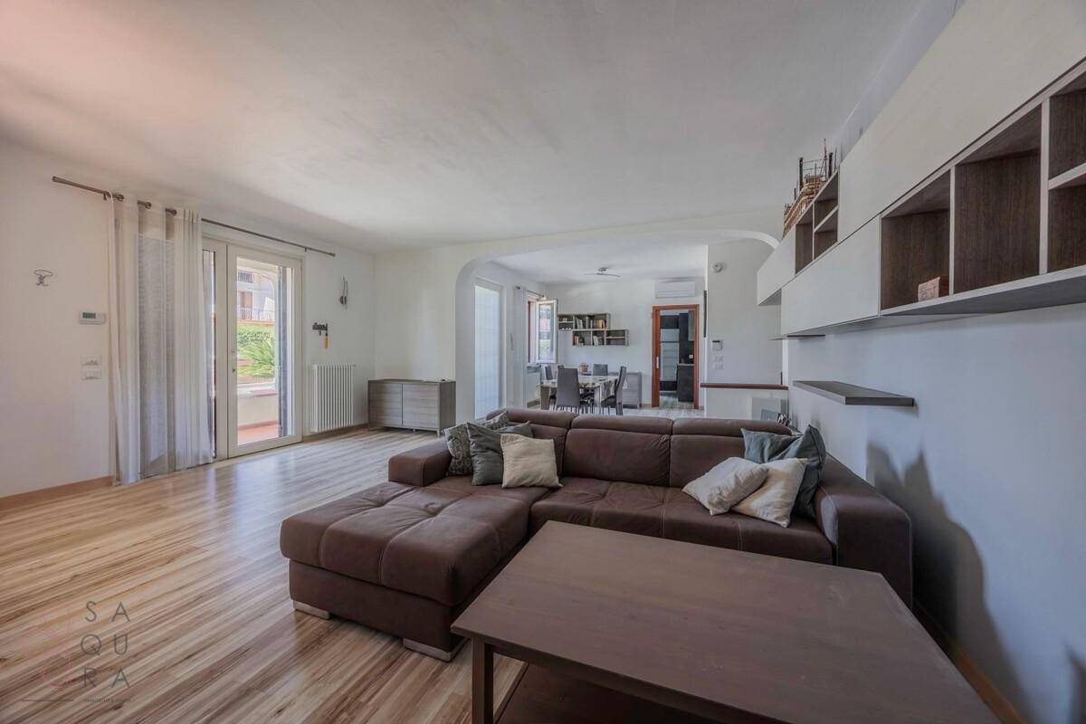 Helles Wohnzimmer mit modernem Sofa, Holzfußboden und Zugang zu einem Essbereich.