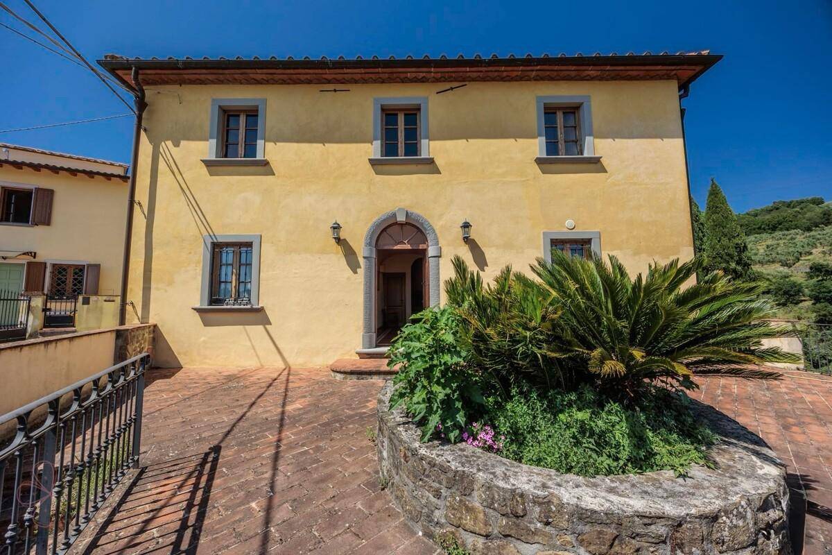 Vorderansicht des traditionellen Landhauses mit ockerfarbener Fassade und gepflastertem Eingangsbereich.