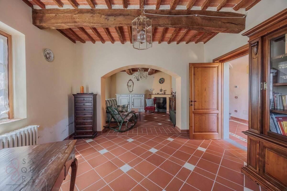 Wohnzimmer mit Terrakottafliesen und Holzbalkendecke, offen zu einem weiteren gemütlichen Bereich.