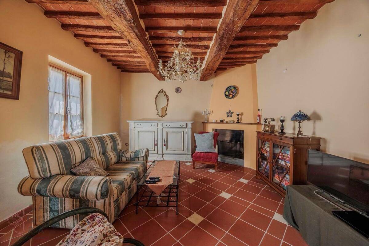 Gemütliches Wohnzimmer mit Kamin, Terrakottafliesen und rustikaler Holzbalkendecke.