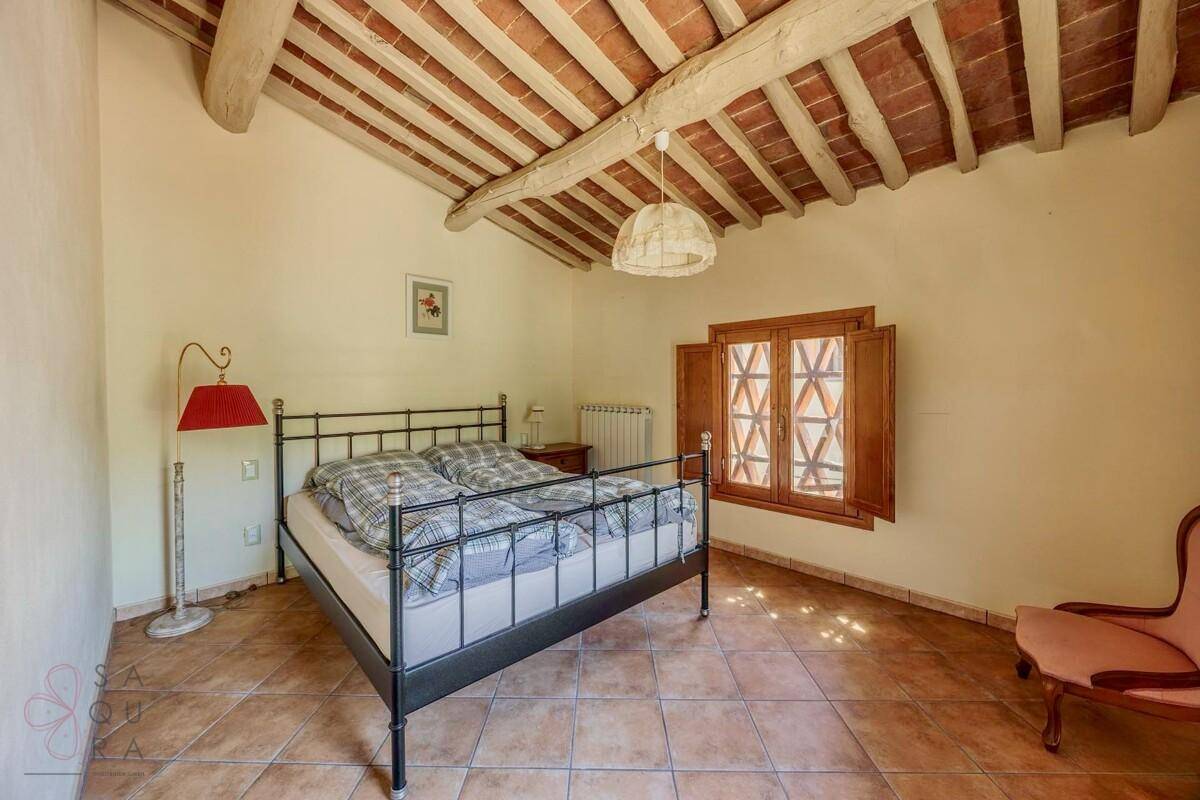 Schlafzimmer mit Terrakottafliesen, Holzbalkendecke und schmiedeeisernem Bett, hell und geräumig.