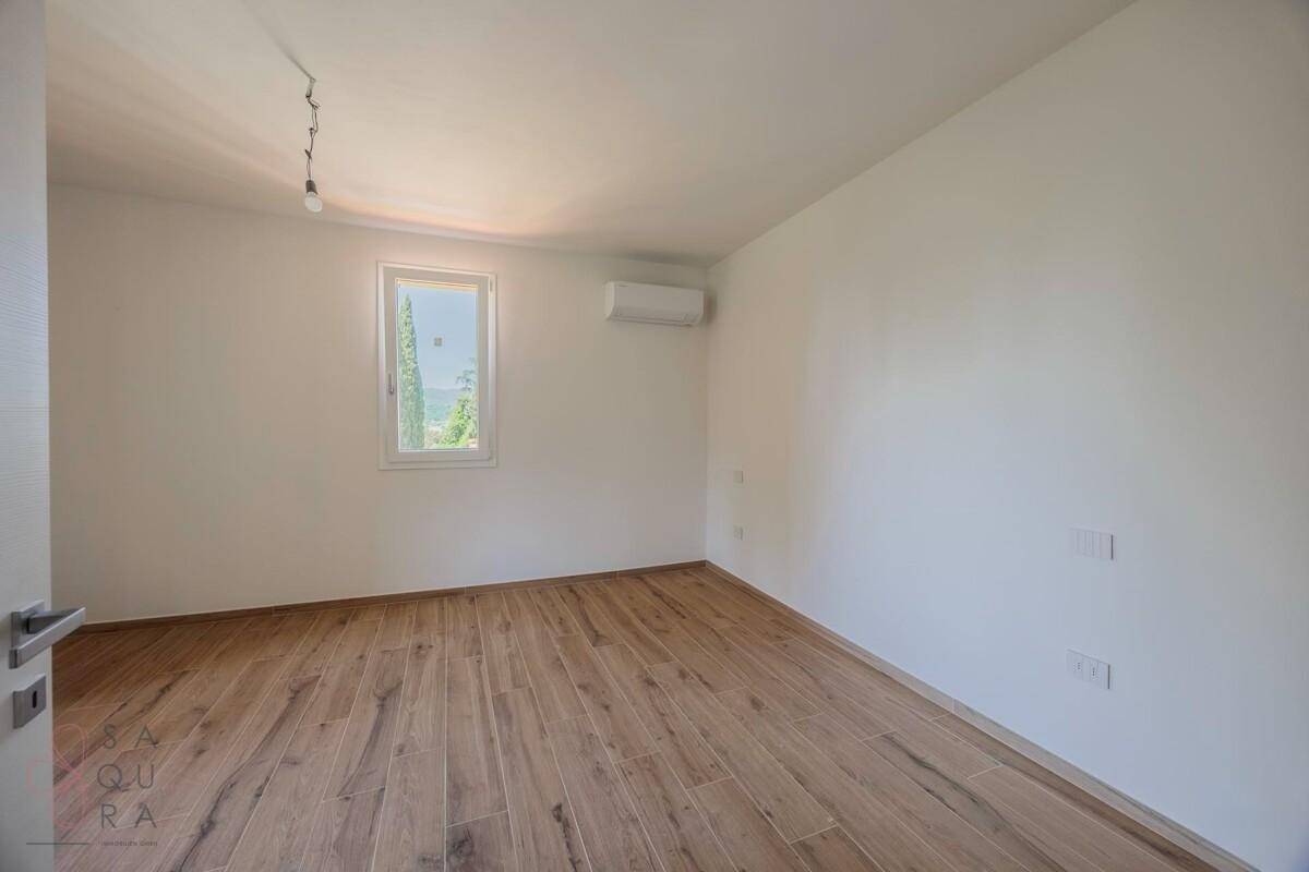 Helles Schlafzimmer mit Holzoptik-Fliesenboden, Fenster und Klimaanlage.