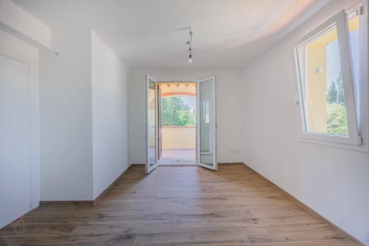 Schlafzimmer mit Holzoptik-Fliesenboden und Doppeltüren, die zu einem Balkon führen.
