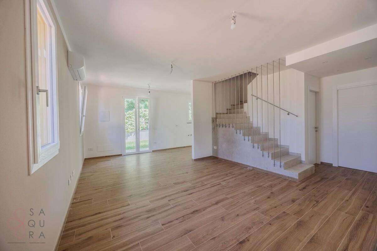 Geräumiges Wohnzimmer mit Holzoptik-Fliesenboden, Treppe und Zugang zum Garten.