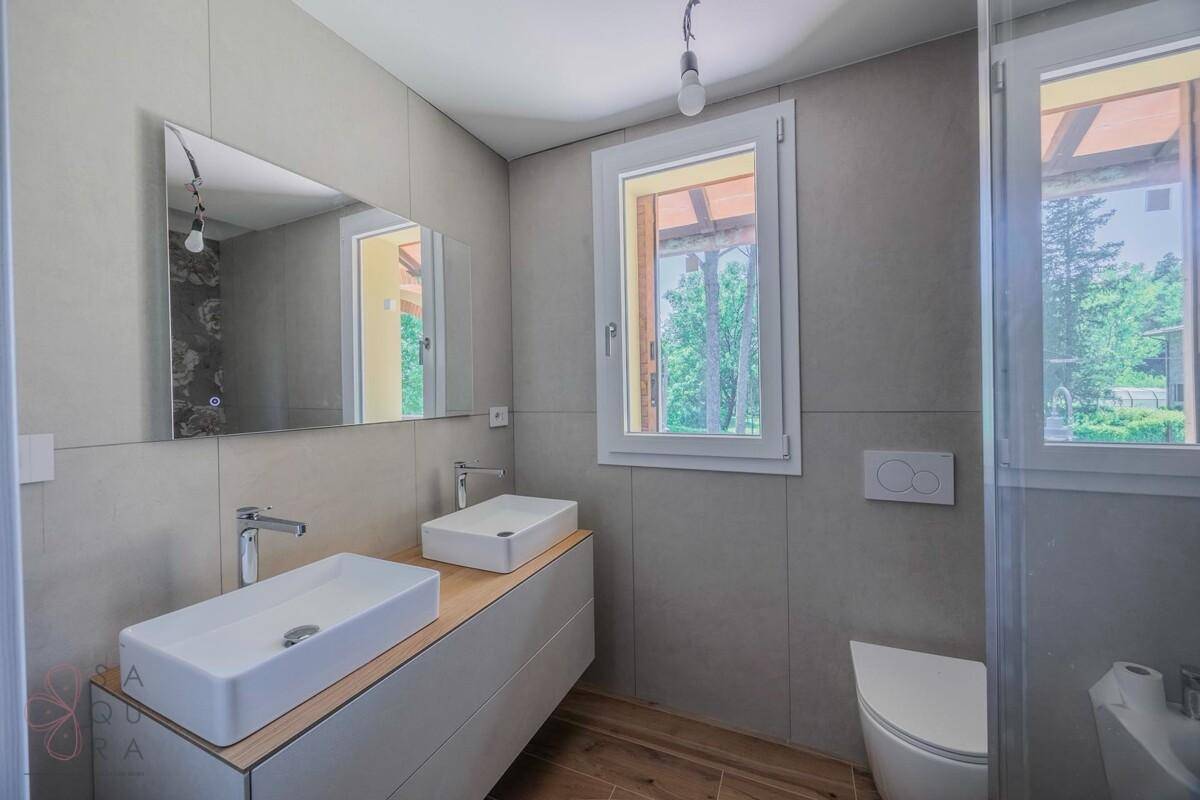 Helles Badezimmer mit Doppelwaschbecken, großem Spiegel und modernen Fliesen an den Wänden.