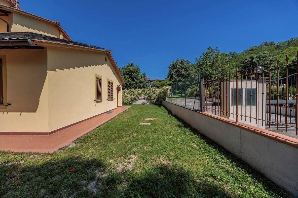 Seitlicher Gartenbereich des Hauses mit Rasenfläche und Metallzaun unter blauem Himmel.
